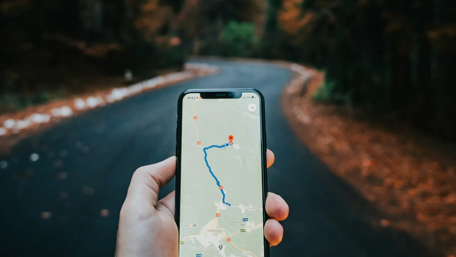 Mão segurando celular com uma rota desenhada no mapa, numa estrada
