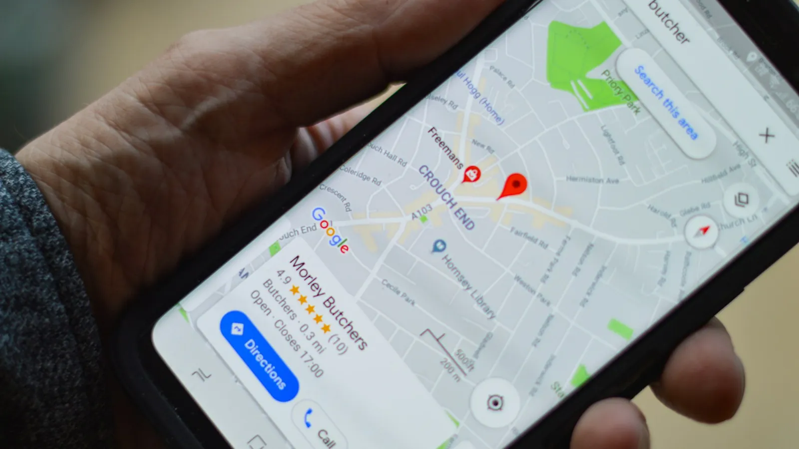 Mão segurando celular com o Google Maps aberto mostrando comércios e avaliações na região